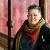 alex bayley - transgender advocate - standing against a fence wearing a rainbow scarf
